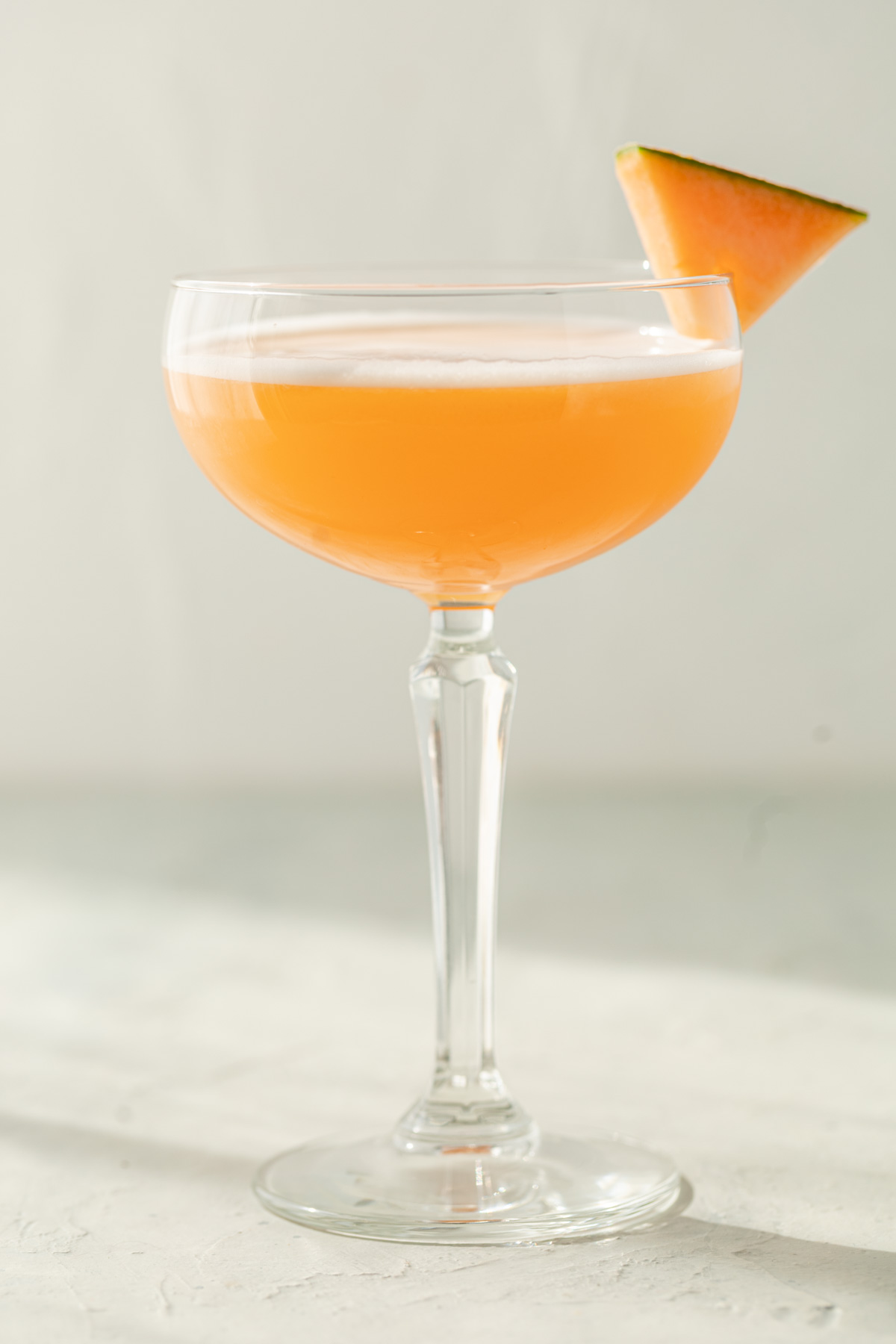 cantaloupe cocktail in coupe glass with slice of melon