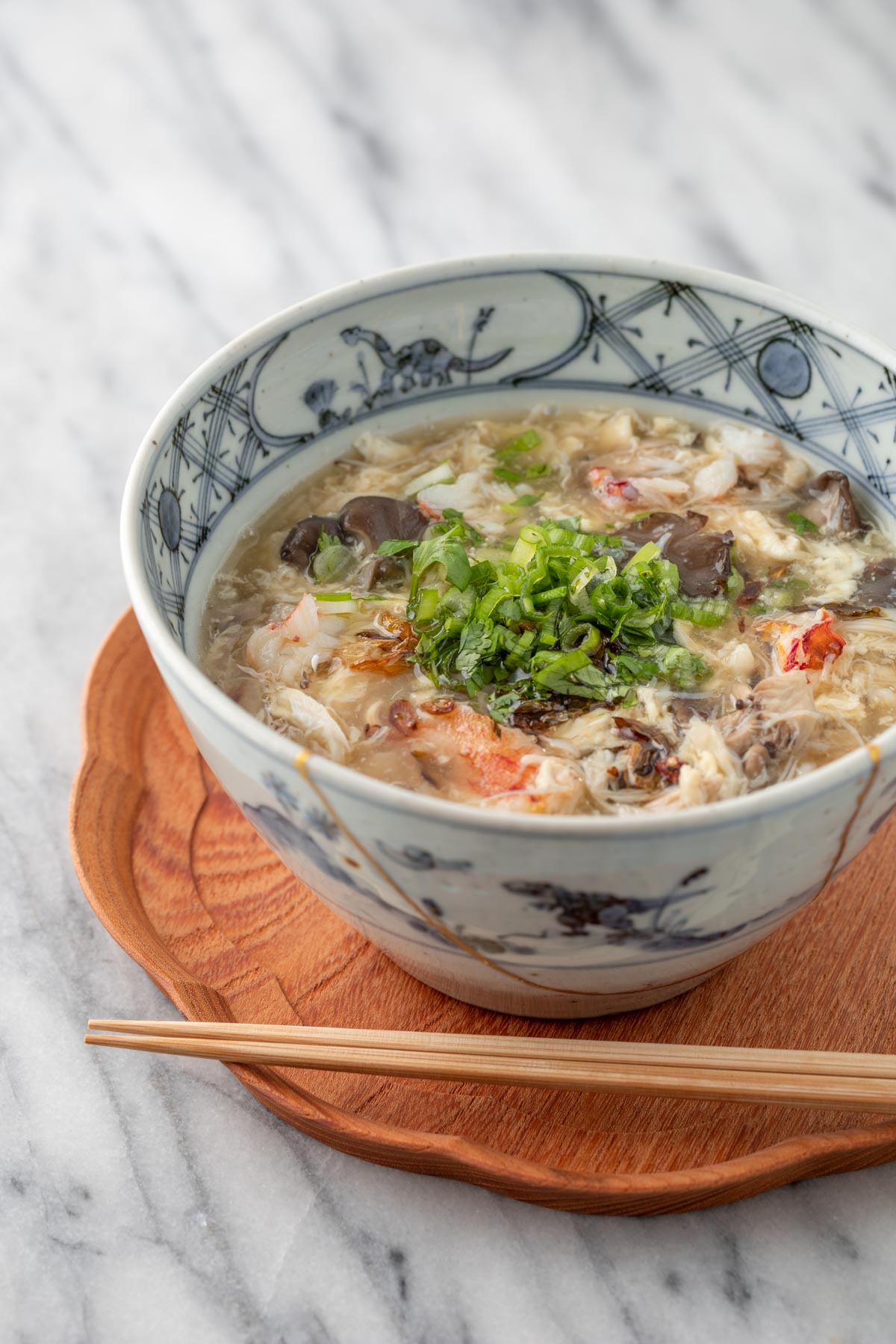 egg drop crab soup with mushroom in a soup bowl with chopsticks and wooden tray