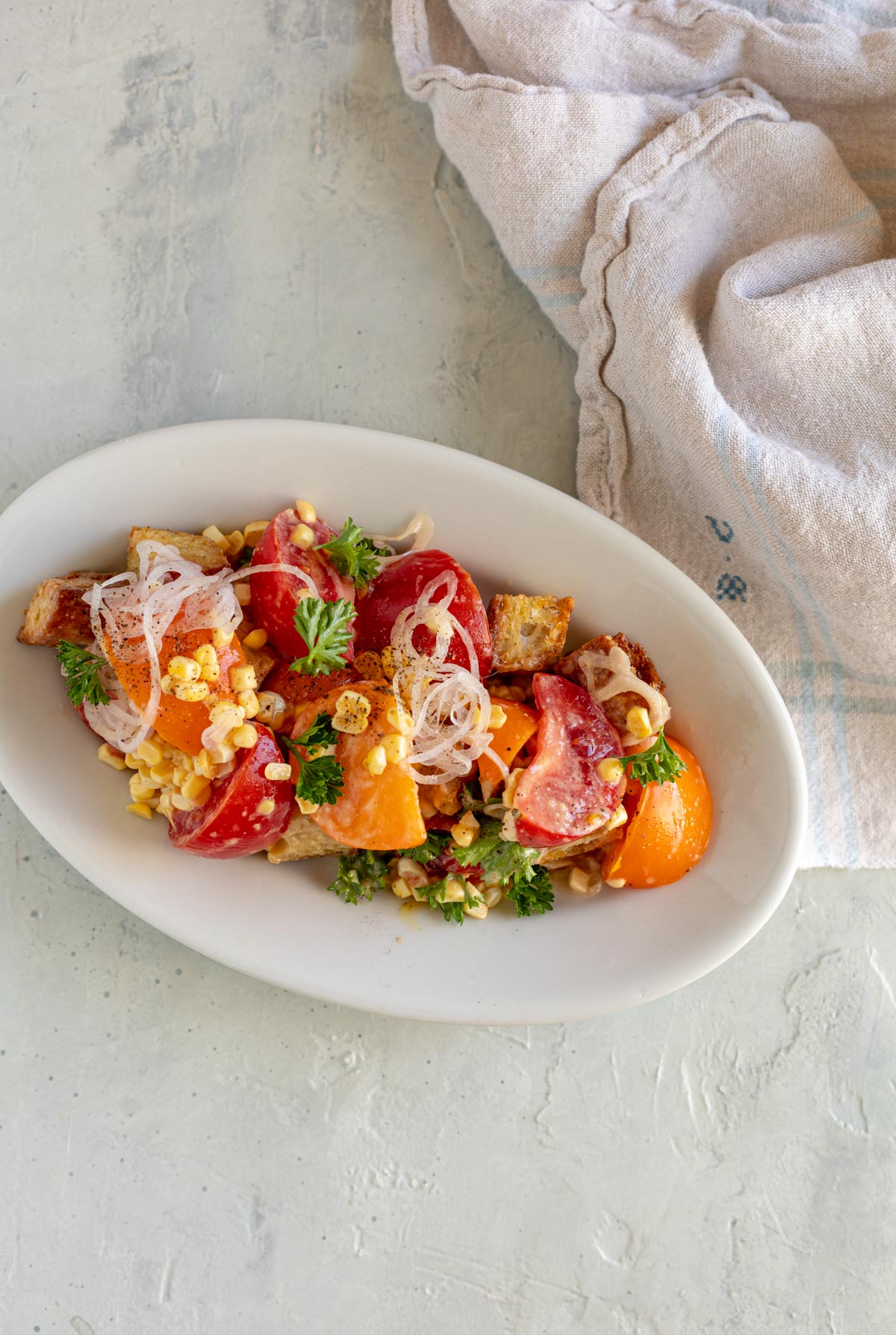 tomato corn salad qith miso anchovy dressing on oval plate with a napkin